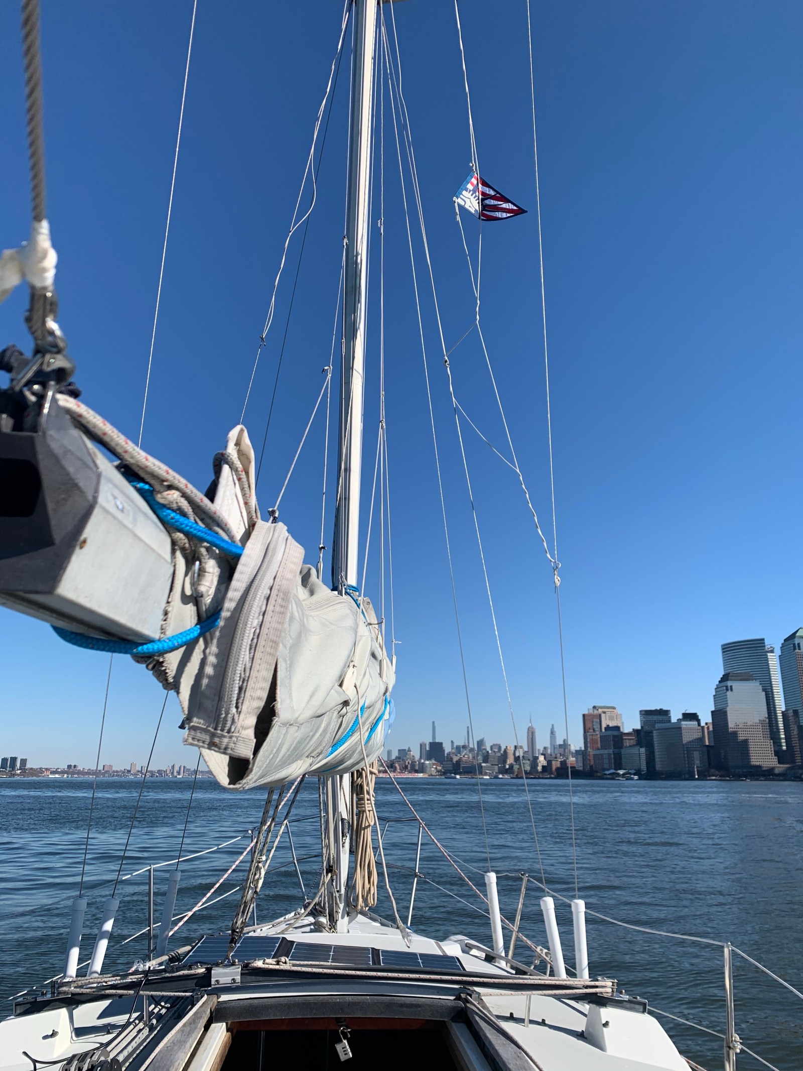View from a sailboat on the harbor, mast and rigging against a blue sky with the city skyline behind